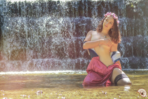 Girl in German Dirndl Dress and stockings undressing in front of a waterfall