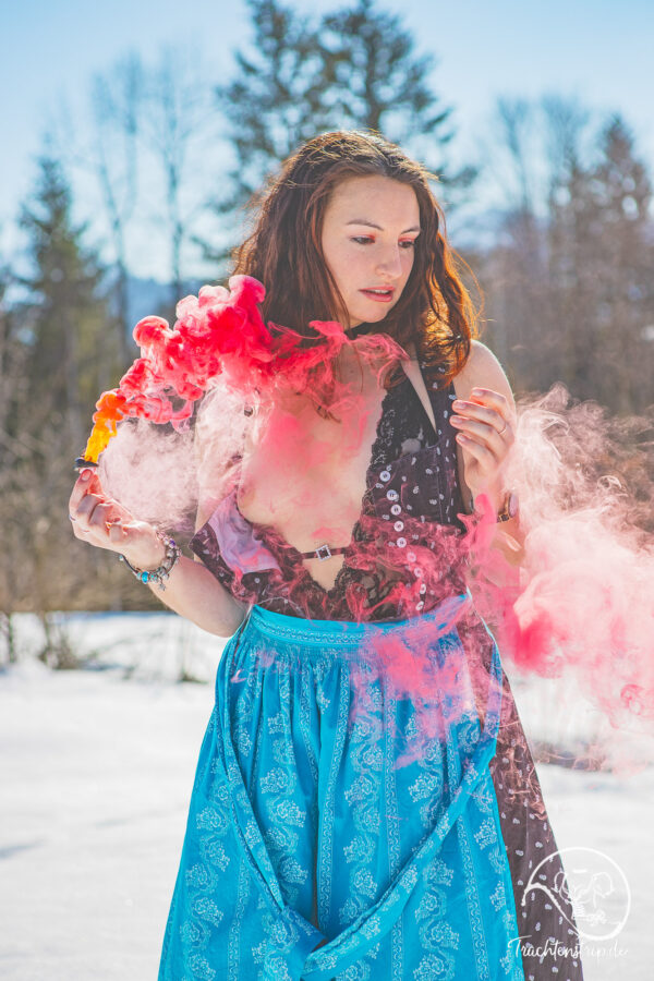 Junges Mädel im Dirndl mit Rauchbombe im Schnee