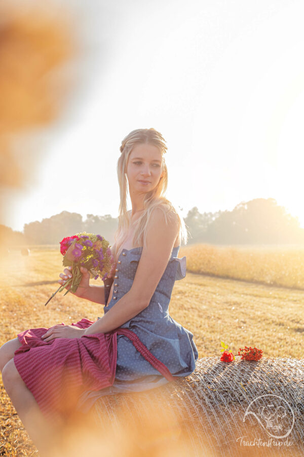 Beautiful blonde sits with opened dirndl on hay bale