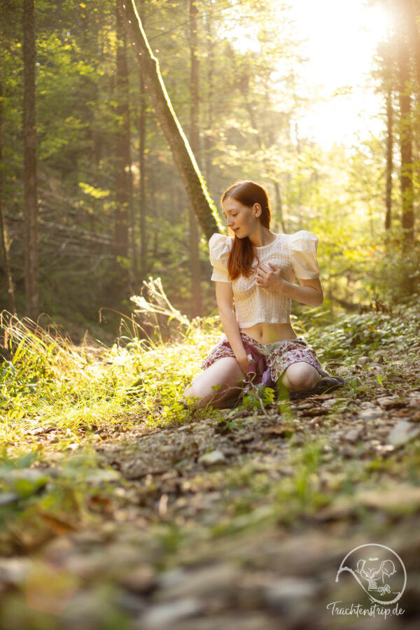 Dirndl Strip: Schöne rothaarige Bavarian Beauty mit durchsichtiger Bluse und Dirndl sitzt im Wald